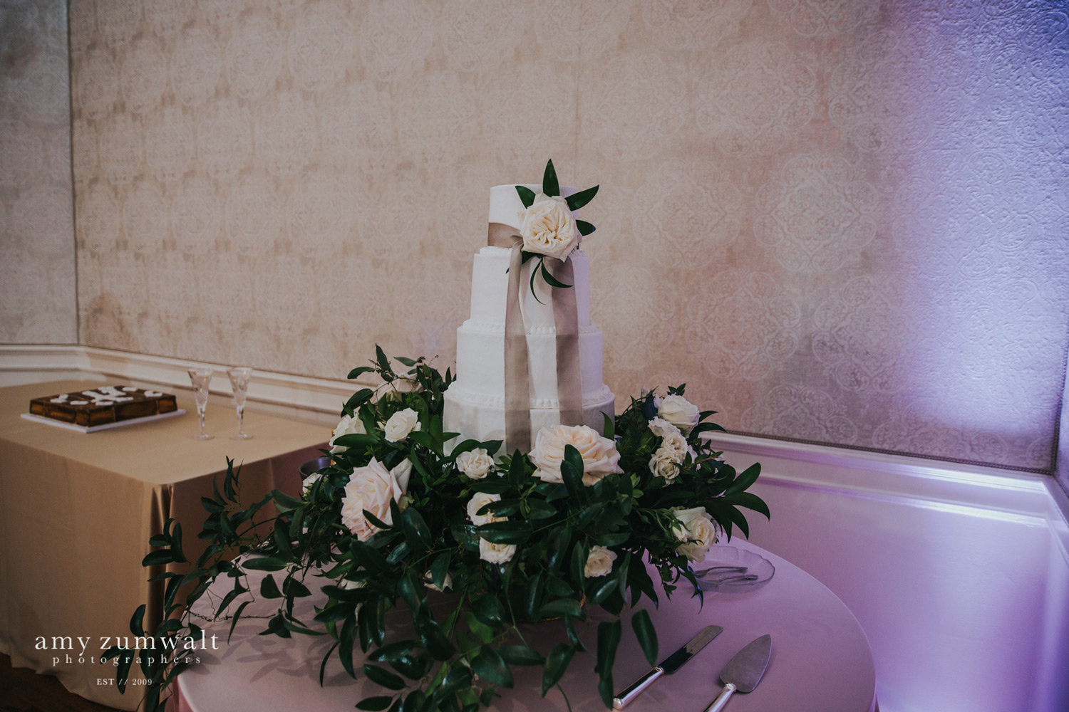 White wedding cake with taupe ribbon and greenery cake stand