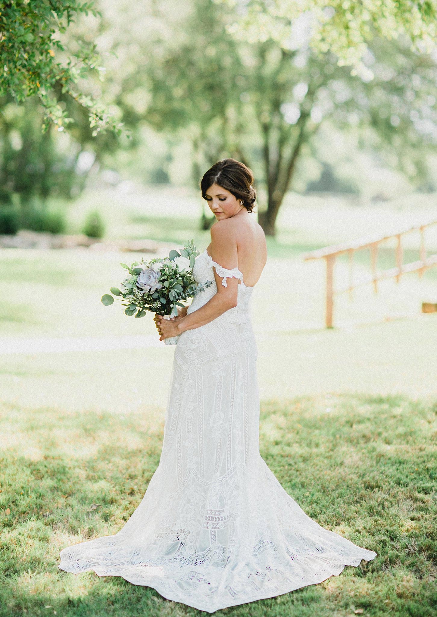 Bride in boho lace dress holding a light greenery bouquet