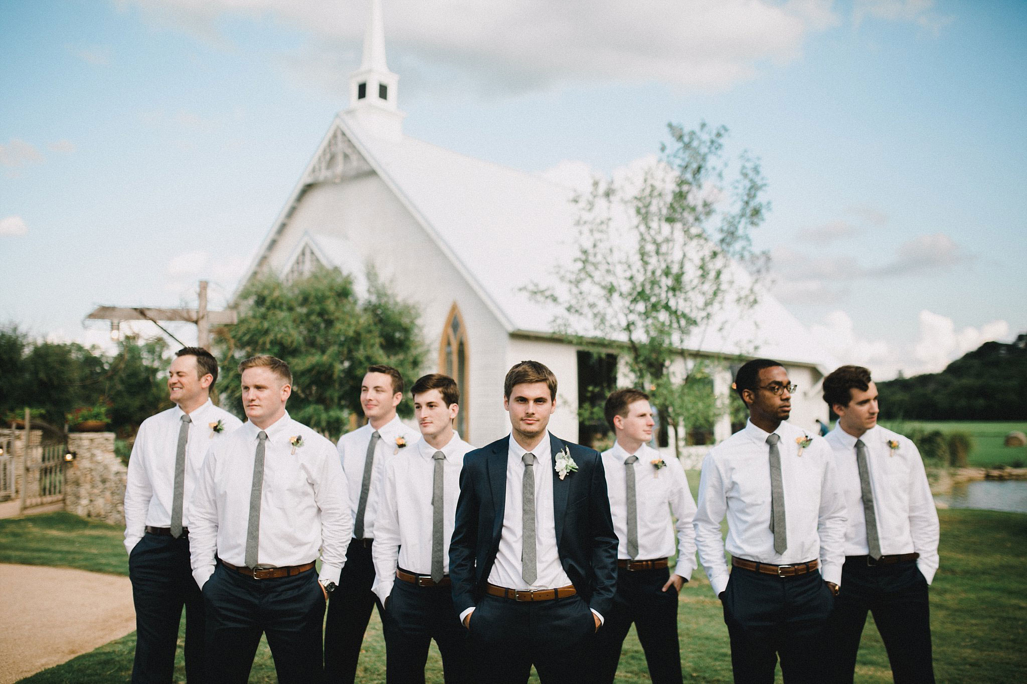 Groom wearing a navy suite with a jacket, and the groomsmen wearing a white shirt and navy pants