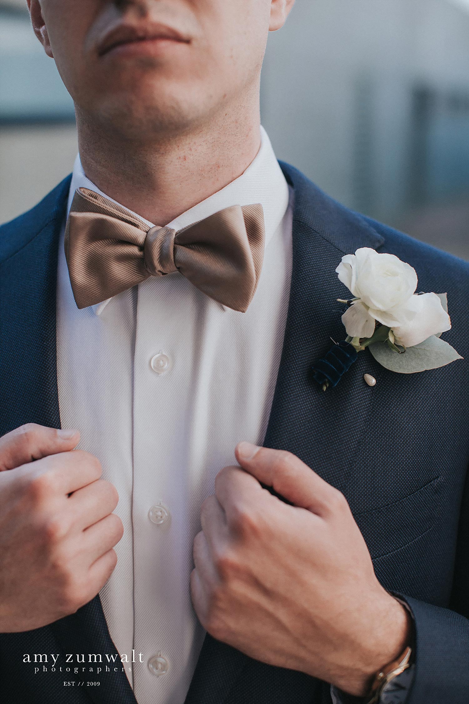 groom wearing a navy suit and bowtie with a velvet ribbon boutonniere