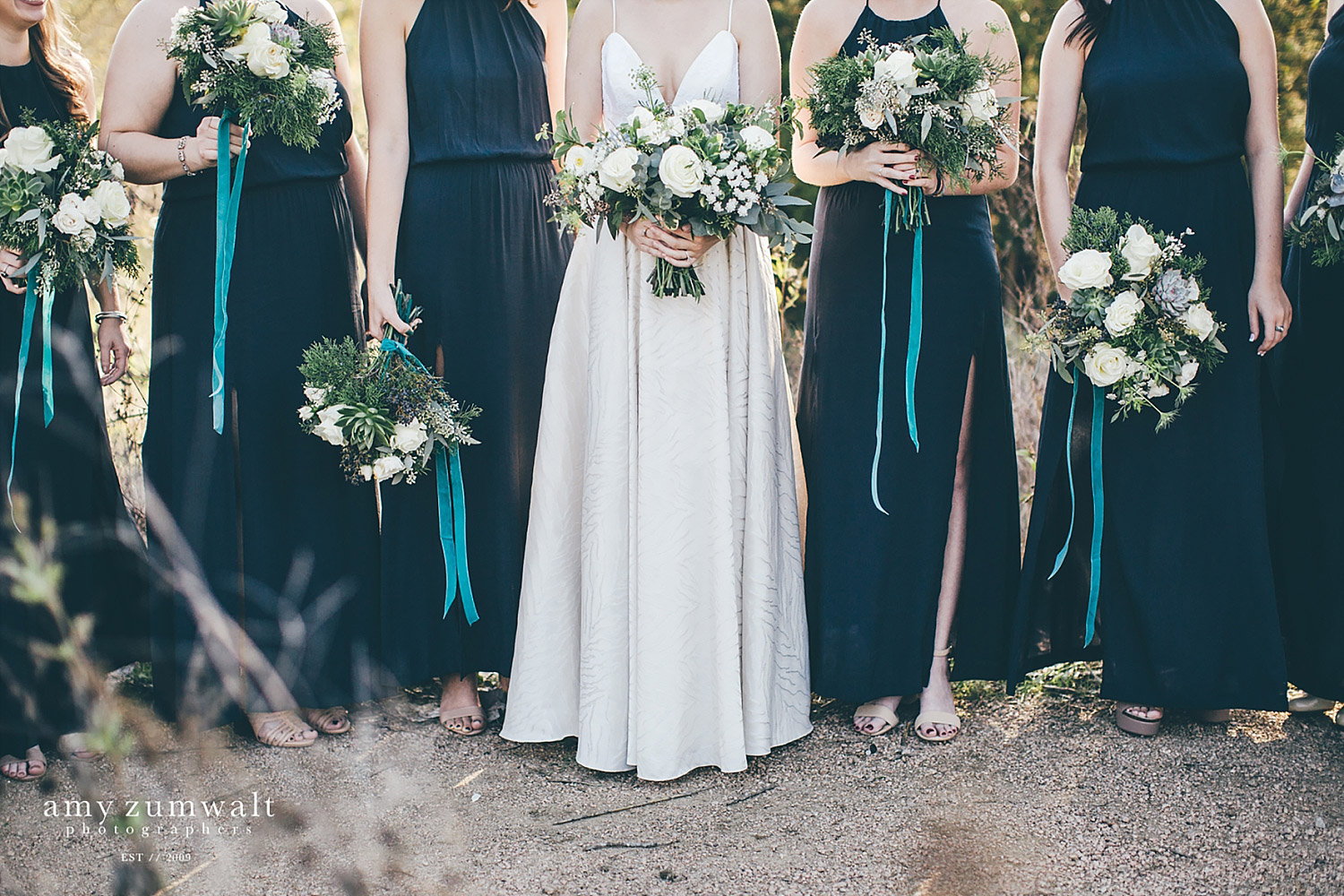 Bridesmaids in low navy dresses with velvet hanging ribbon from their greenery bouquets