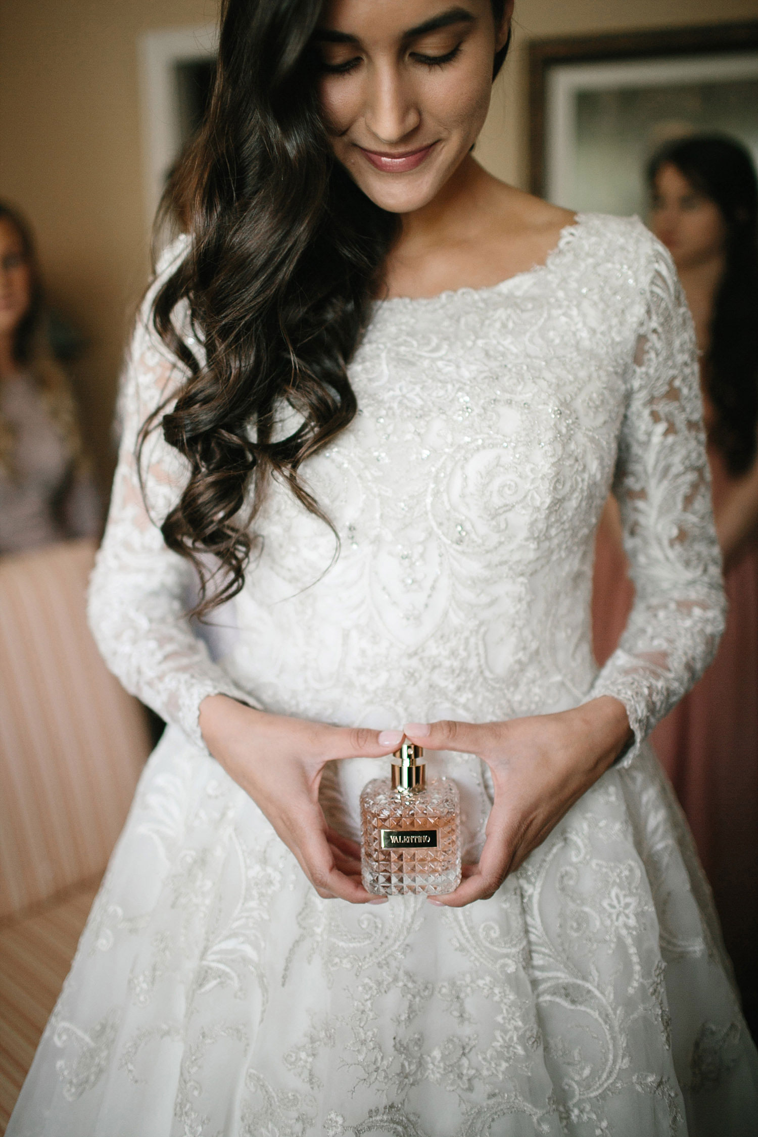 Bride in long sleeve lace dress holding a perfume bottle