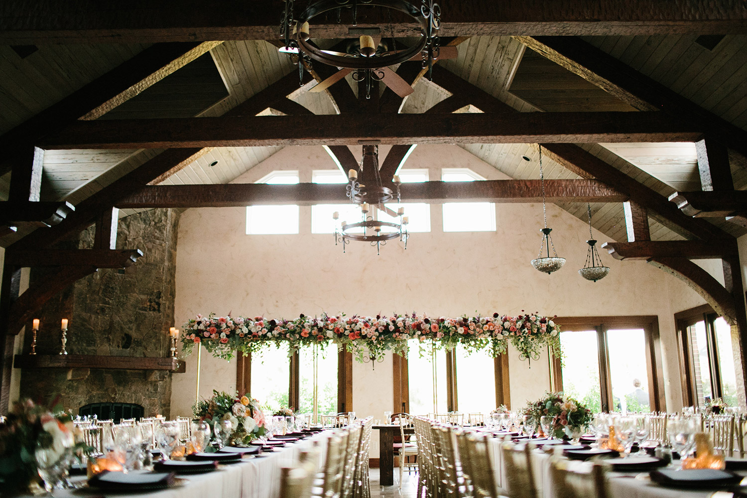 Wedding reception with large wood beams and tall floral hanging centerpiece