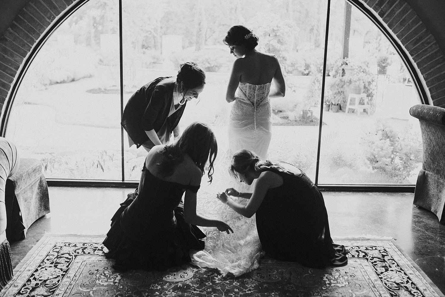bridesmaids putting on the brides dress in a black and white photo