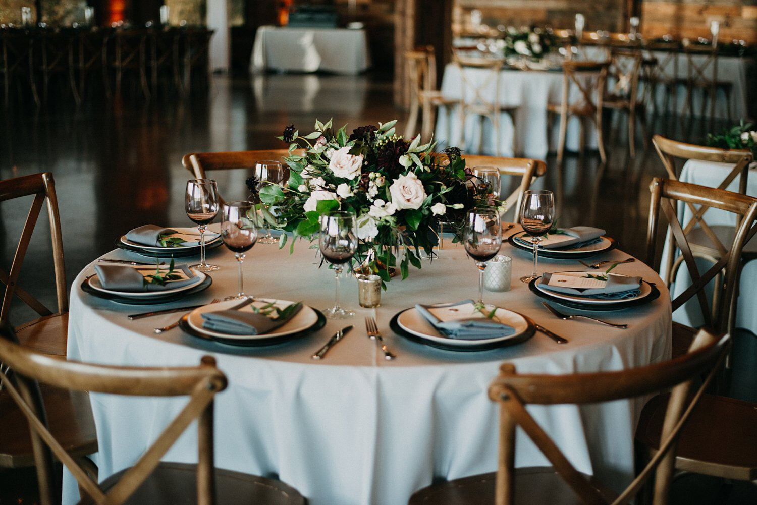 Table with a grey linen, black chargers &amp; white flowers in rustic barn