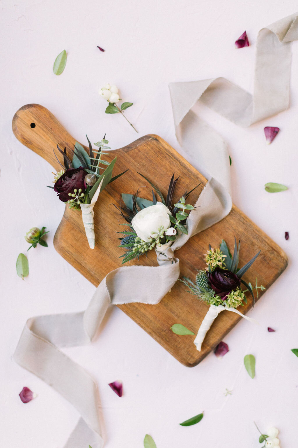 Boutonnieres on a wood cutting board with grey ribbon