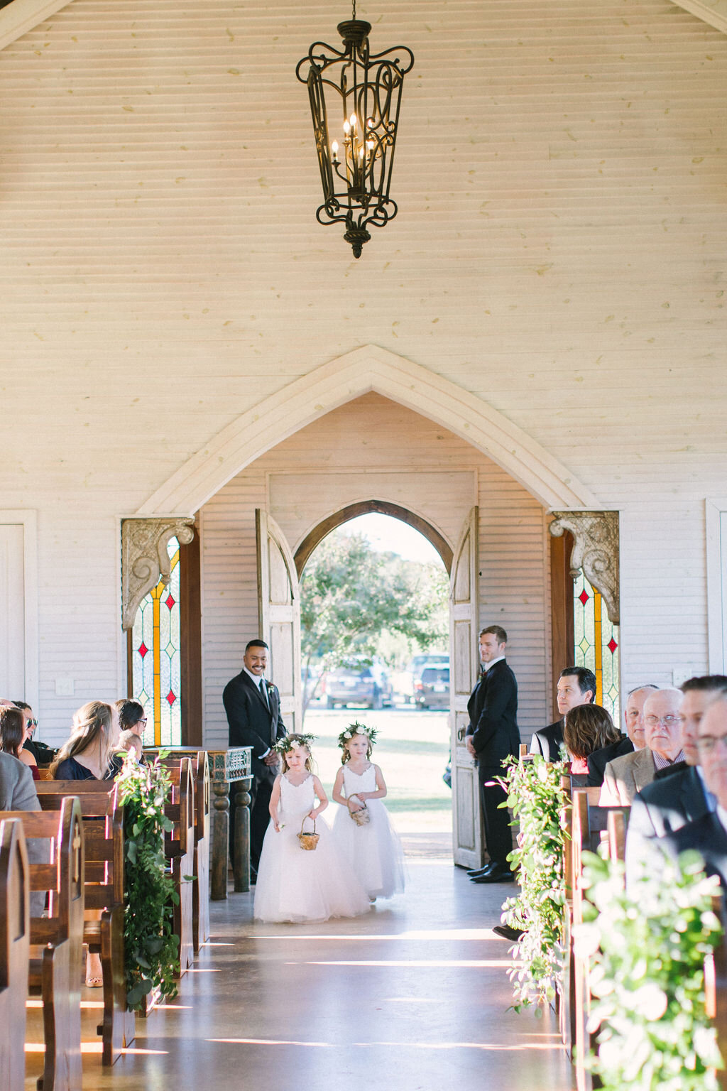 Flower girls walking down the aisle at Texas white chapel ceremony