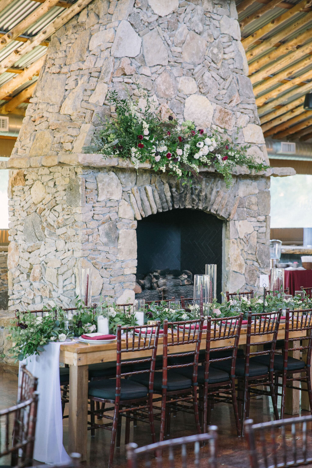 Large wood fireplace with a asymmetrical greenery installation on the mantel with a wood farm table 