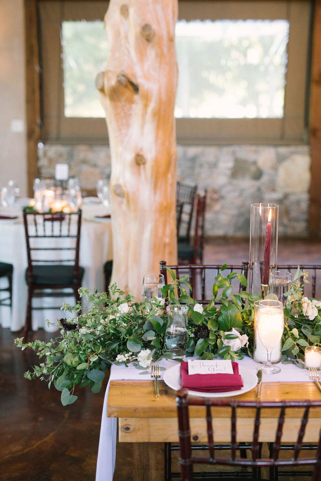 Tablescape with a large greenery garland &amp; burgundy napkin.