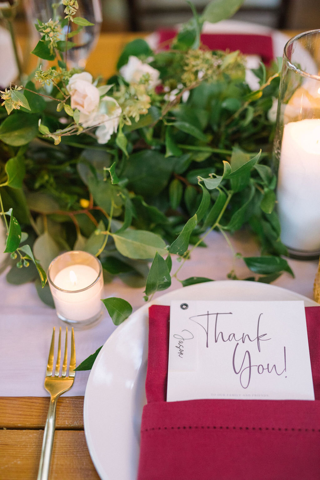 Burgundy hemstitched napkin place setting with a greenery runner and modern white plate