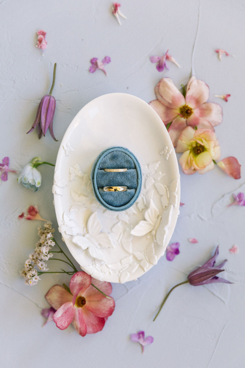 Velvet blue ringbox on white plaster dish with pink flower flat lay