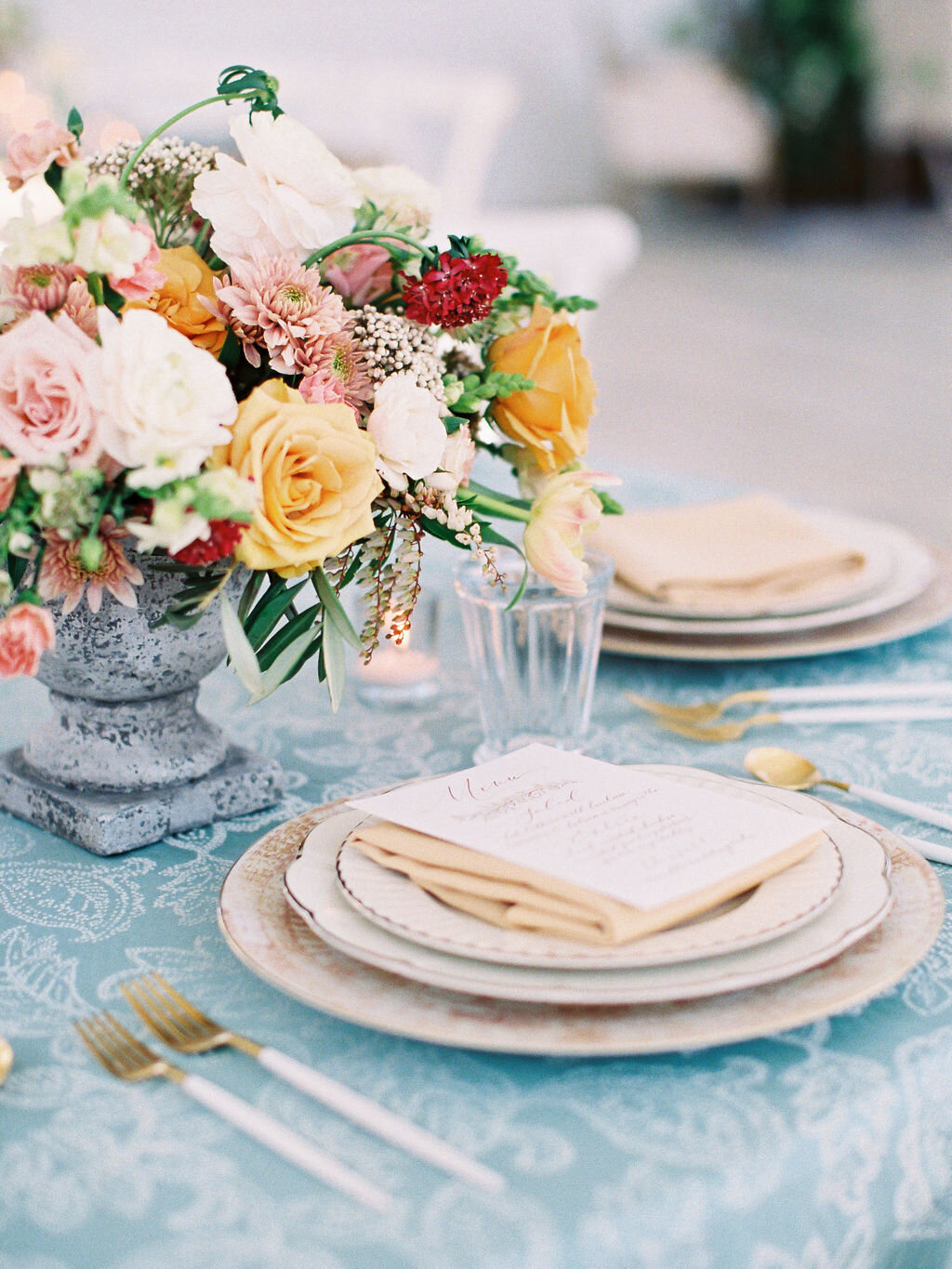Light blue table setting with white flatware &amp; orange, red &amp; pink flower centerpieces