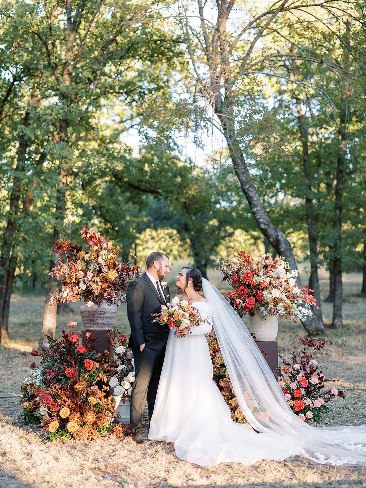 Bride &amp; Groom standing in front of red ceremony flowers at Texas wedding by Ranch wedding planner Shannon Rose Events