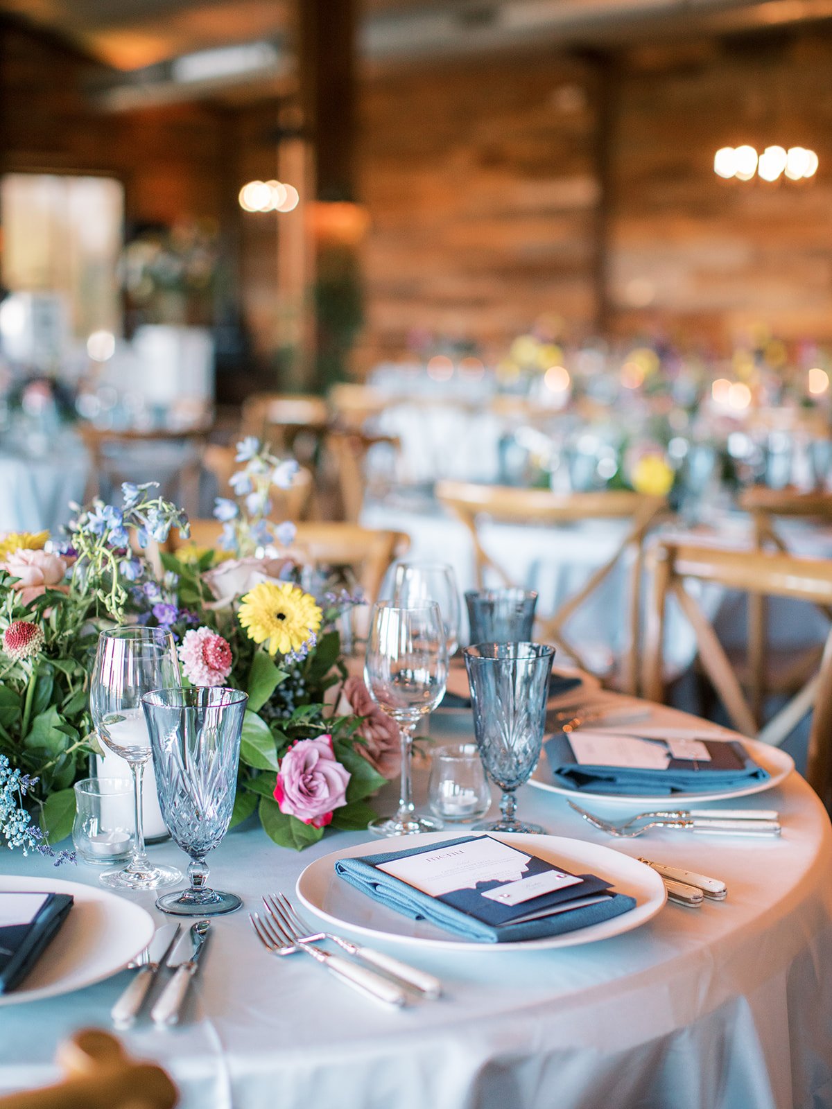 Wedding tablescape with light blue linen, dark blue menu, white silverware and colorful flowers