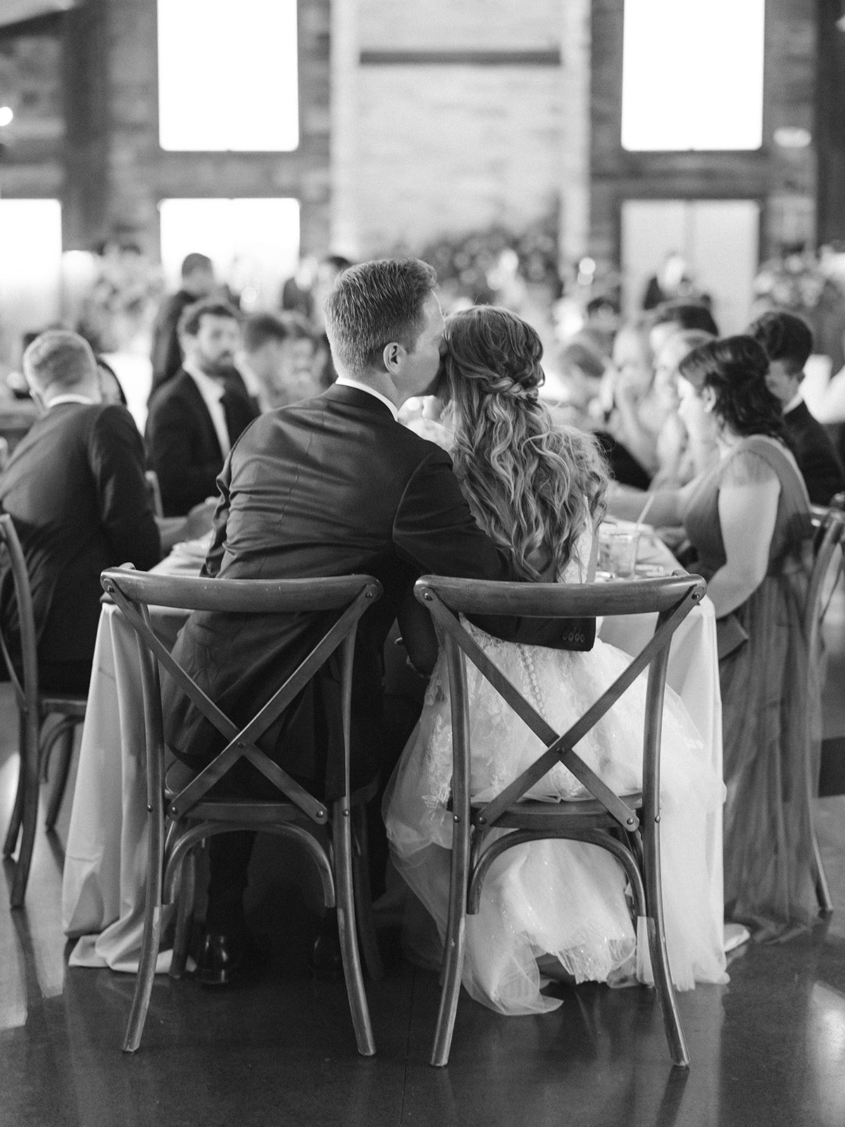 Black and white photo of couple kissing on cross back chairs