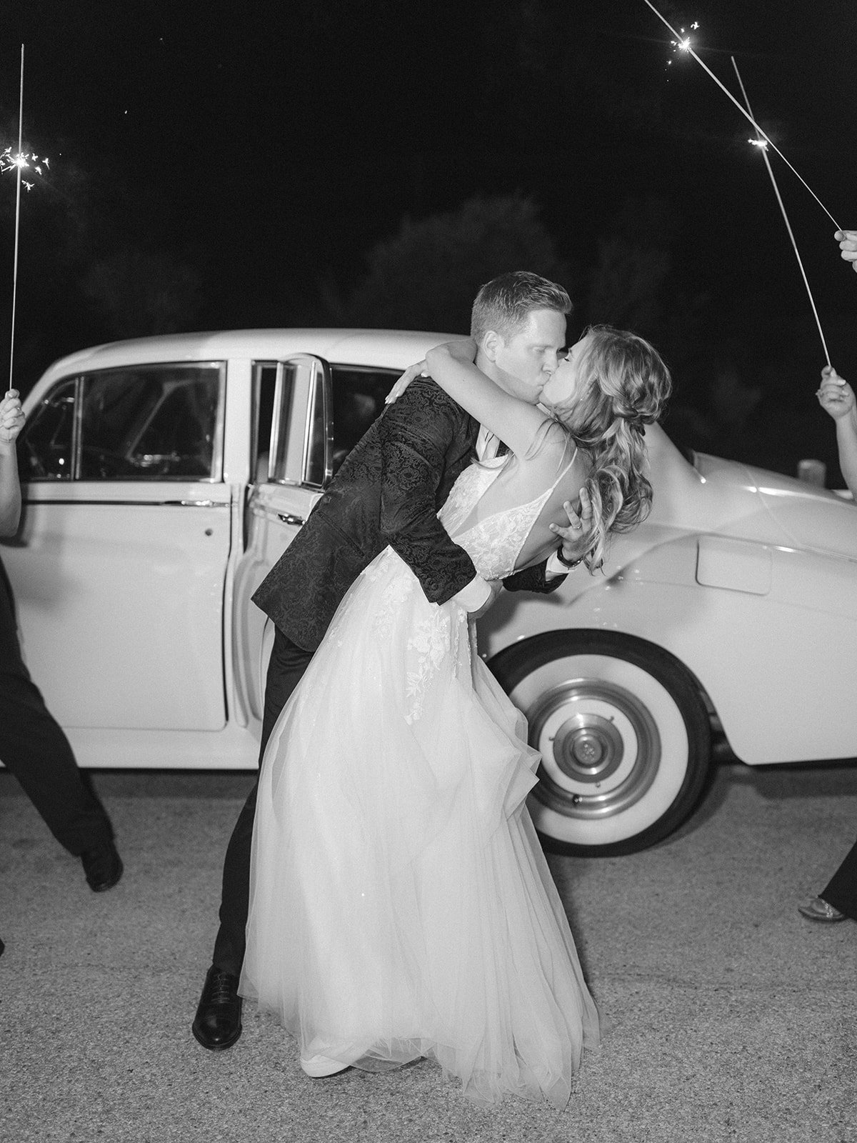 Bride and groom kissing in front of vintage car for wedding send off