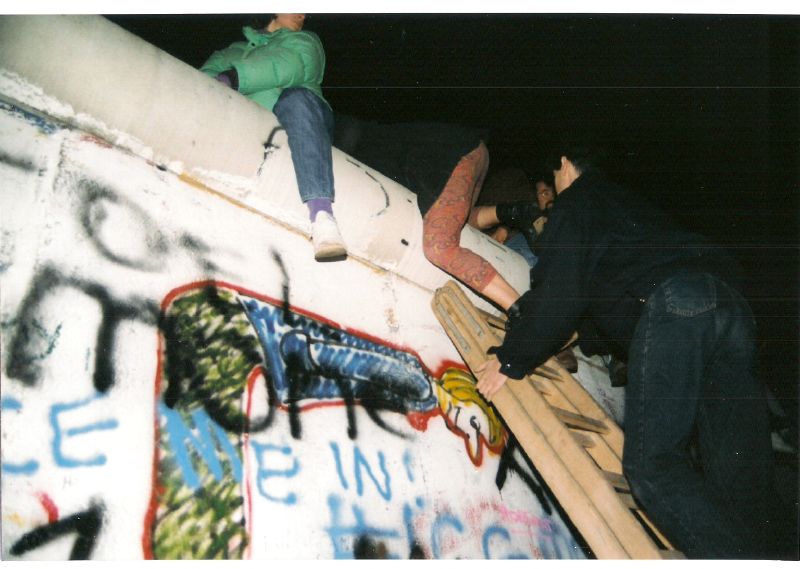 People climbing over a graffiti Berlin wall in 1989.