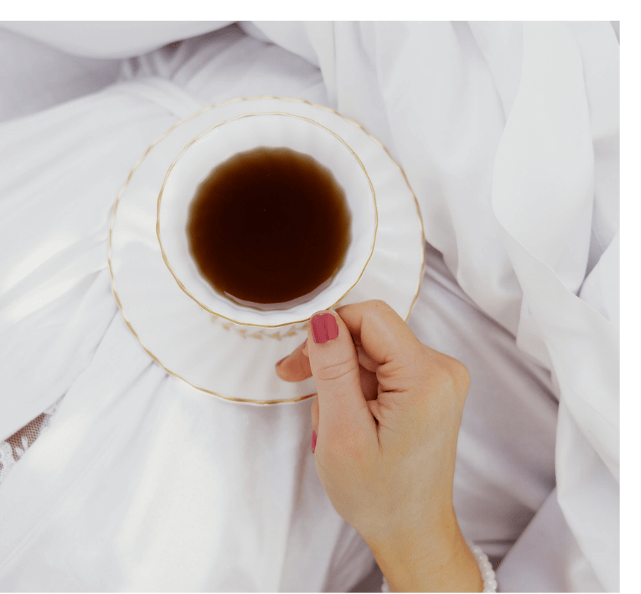 tea cup being held over white bed