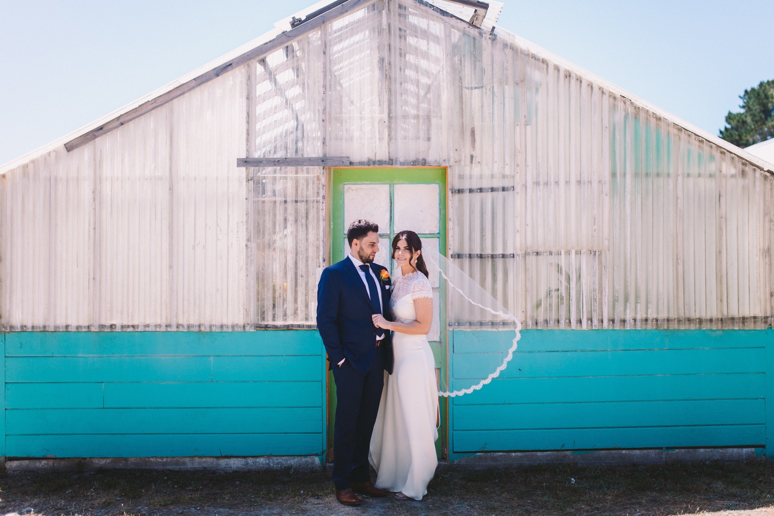 Bride & Groom Portrait in front of Brightly Painted Greenhouse at Shelldance Orchid Gardens