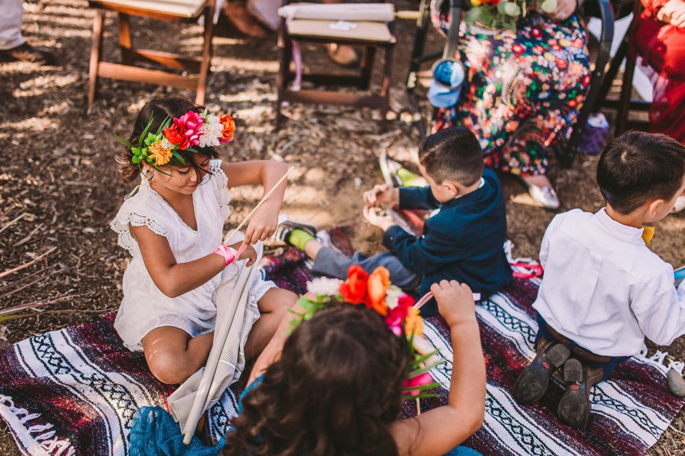 Flower Girls &amp; Boys Watch Ceremony From Colorful Blanket Next to Wedding Arch