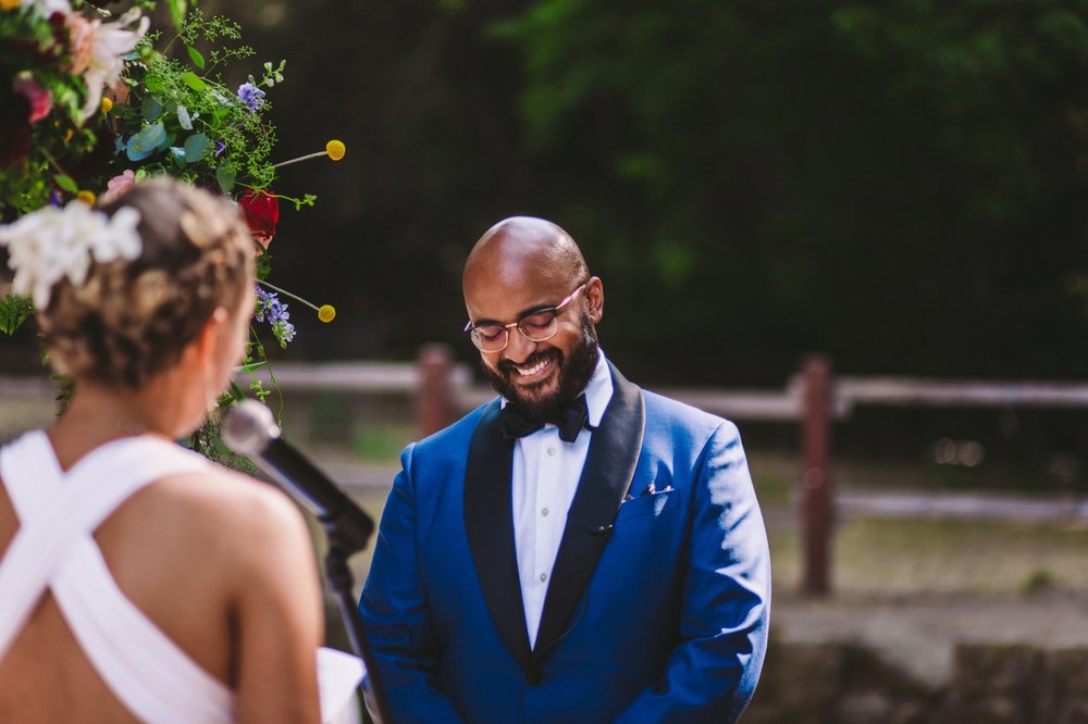 Photo of Groom Smiling as Bride Reads Vows during Sanborn County Park Ceremony 