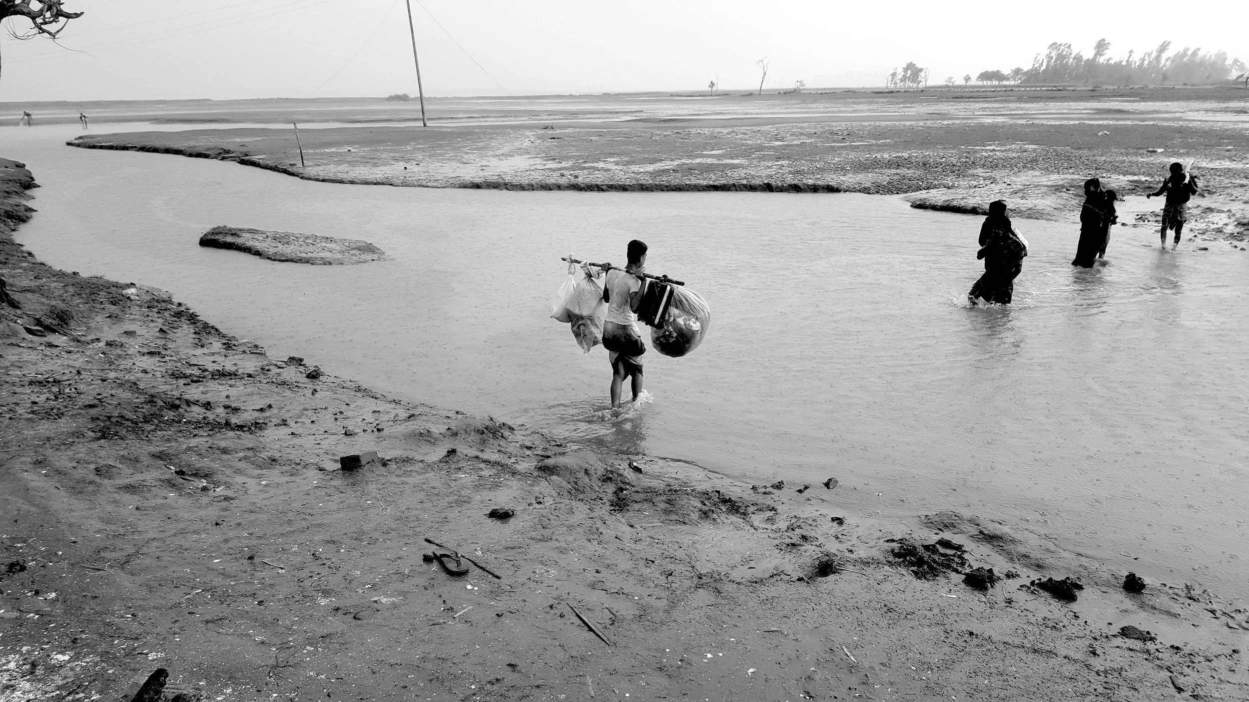 Rohingya carrying their belongings over harsh terrain. Many Rohingya refugees are forced to walk through sites clustered with landmines in order to reach safety. This group crossed the border and arrived on the shores of Bangladesh at 4 am. They are fortunate compared to the nearly four thousand Rohingya stuck at the border of Myanmar.