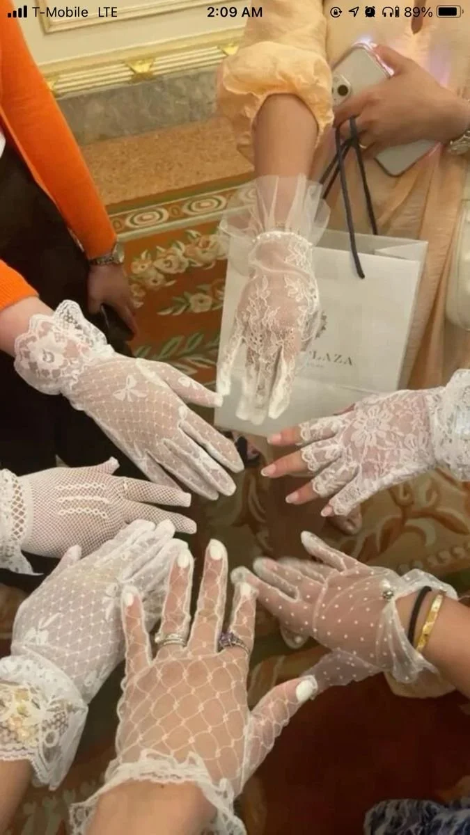 Multiple people wearing white lace gloves forming a circle with their hands on a table.
