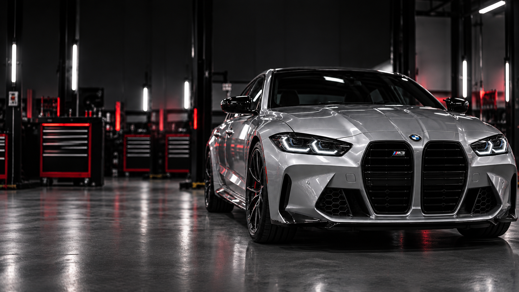Silver BMW M3 in a dark automotive workshop with red tool cabinets