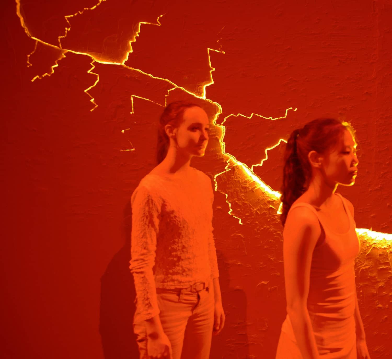 Two performers standing in front the glow coming from the cracked wall.