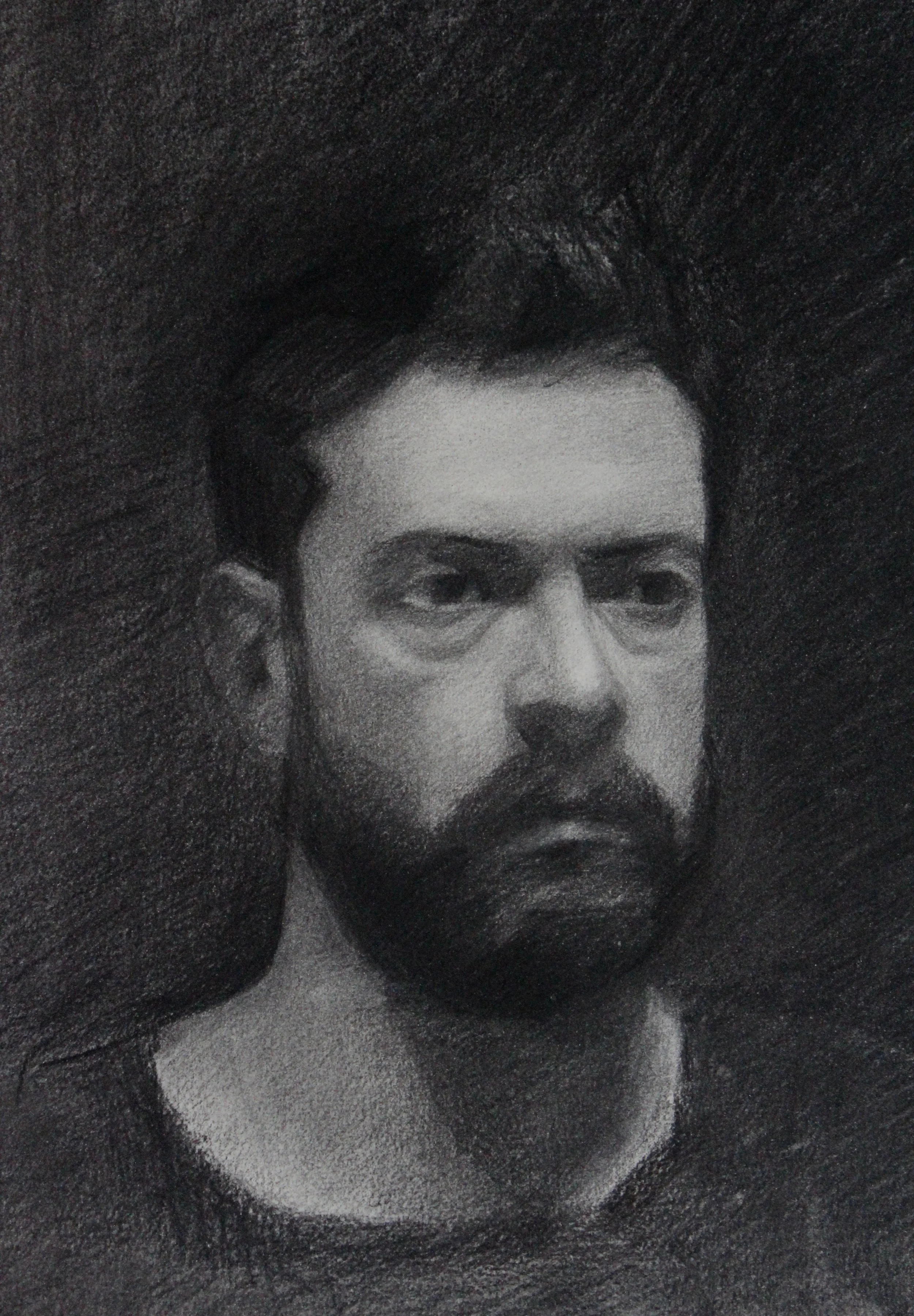 A black and white charcoal drawing of a man with dark hair and a full beard, looking slightly to the side.