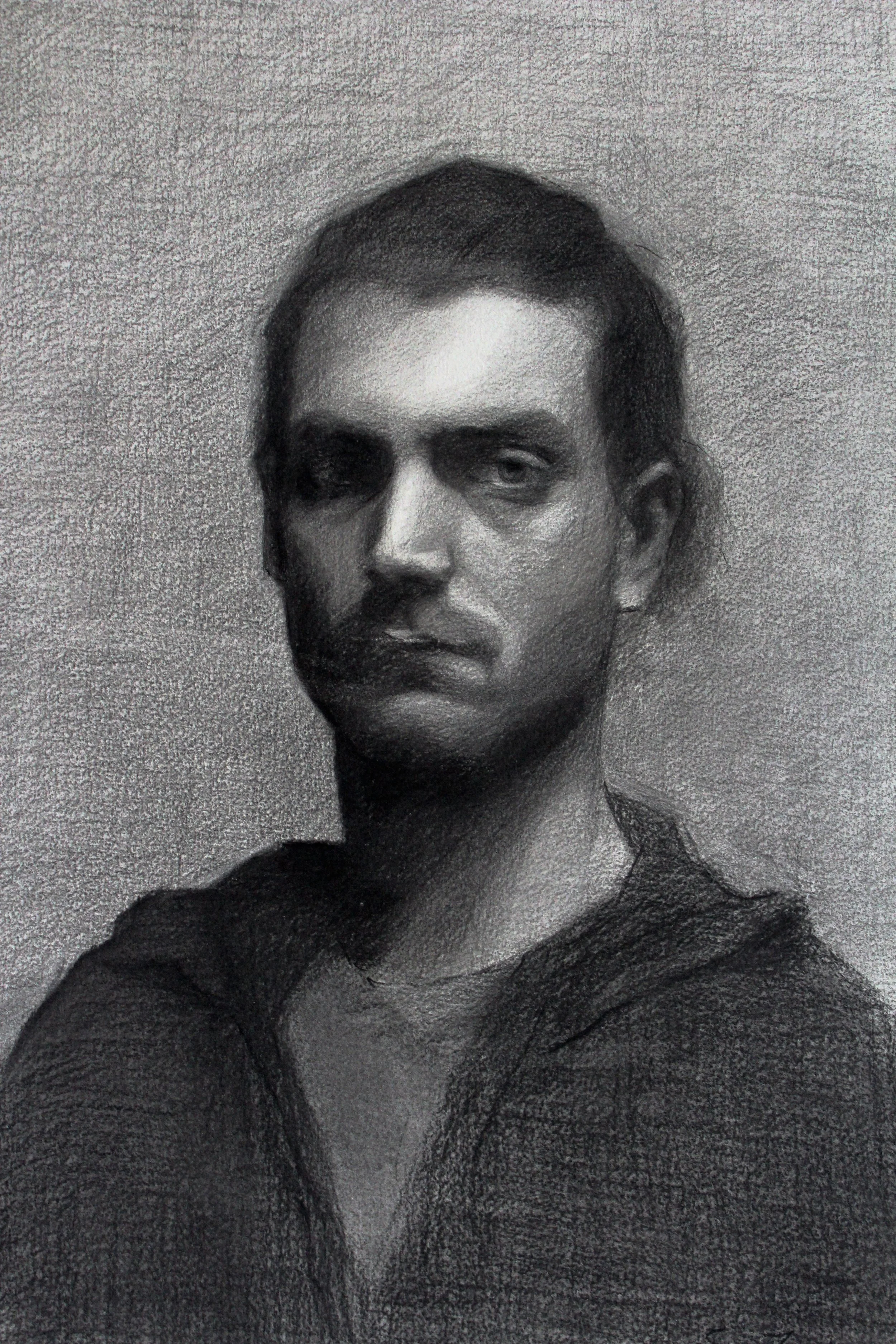 A charcoal portrait of a young man with hair pulled back and up, looking directly at the camera with a serious expression.