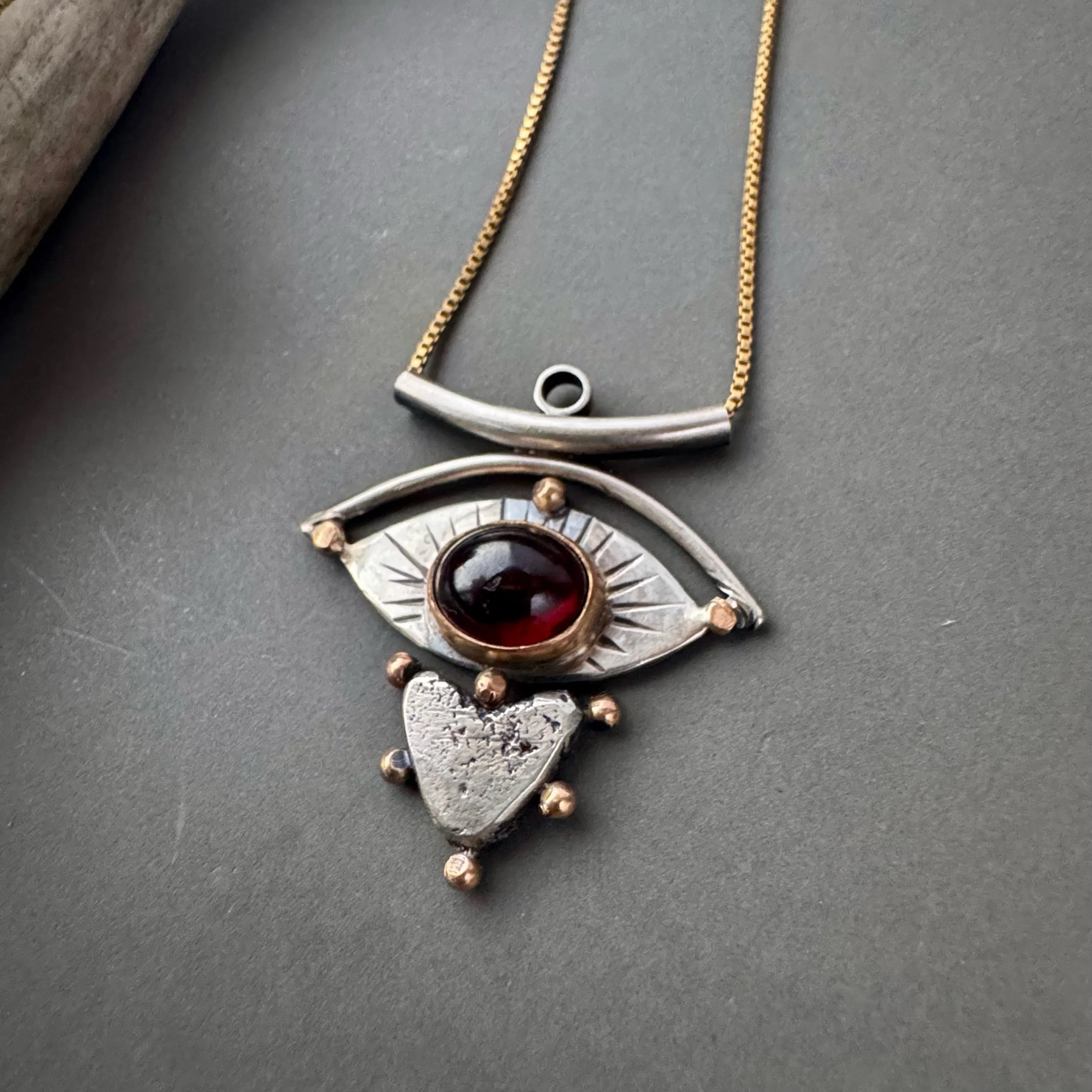 handforged heart and eye necklace with deep red garnet to honor the act of witnessing the world with love and being witnessed with love
