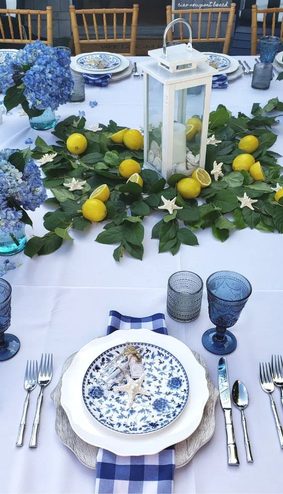 Add a little coastal flair by scattering white starfish around the table on a bed of ivy and white lanterns showcasing the centerpiece, then add pops of color to table with fresh lemons-which your guests can you use if serving seafood, and the individual posies filled with light blue hydrangea complete this pretty table. Ciao!Newport Beach .