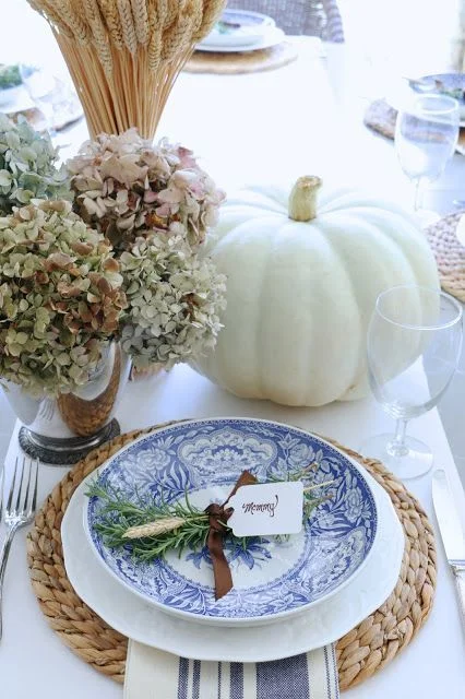 This tablescape is created by the Eleven Gables Blog , how simple and pretty is the fall centerpiece of hydrangeas, white pumpkins and a vase filled with a bundle of wheat stems. A crisp and white table runner, showcases the water hyacinth round placemat and the gorgeous blue and white dinnerware. I love the pretty herb + wheat posy place card.