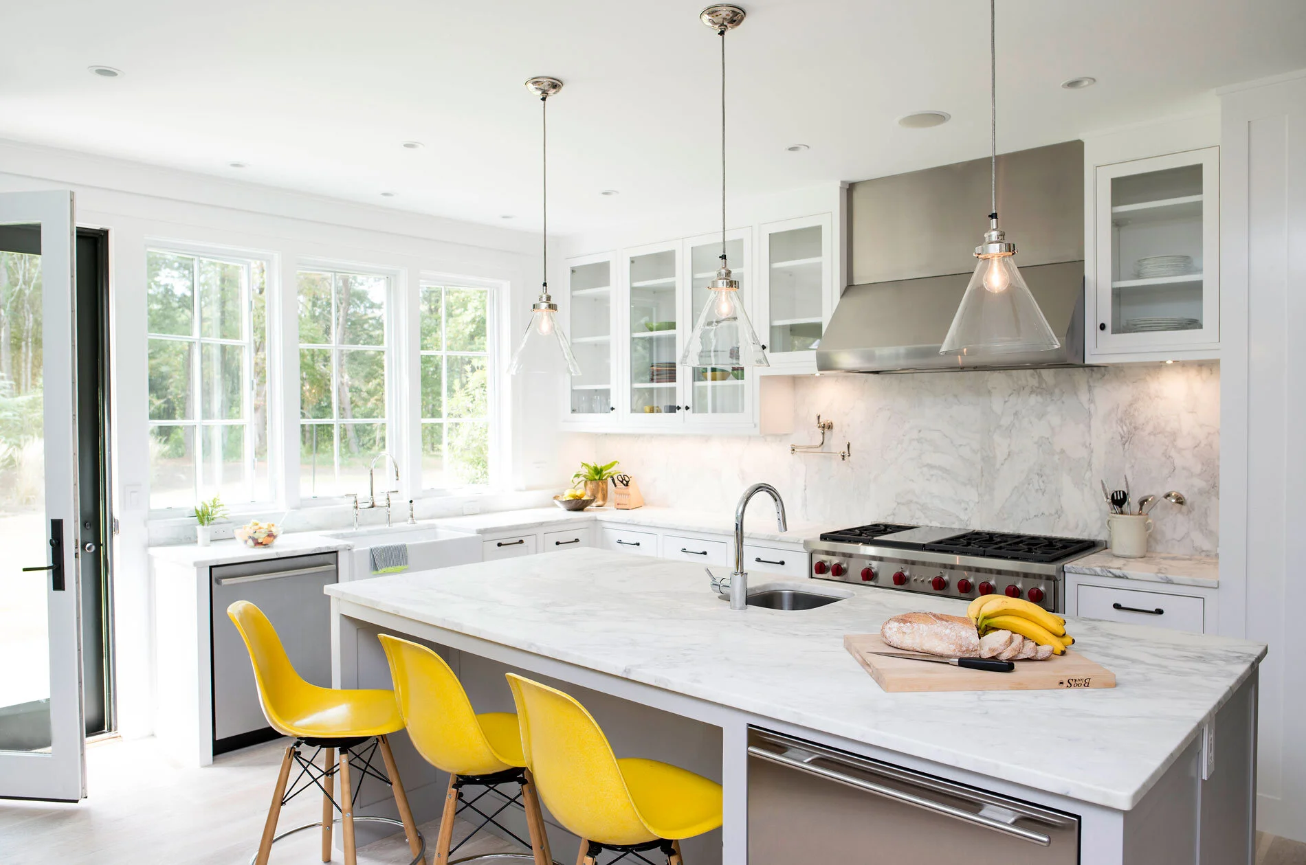 A clean and crisp white kitchen, marble counter tops and stainless steep appliances with a surprise pop of color with the yellow counter stools. I love a wall of windows overlooking the backyard, as your prepping dinner you can keep an eye on your children playing, or just enjoy the daylight. Similar yellow counter stools here and similar pendant light here .