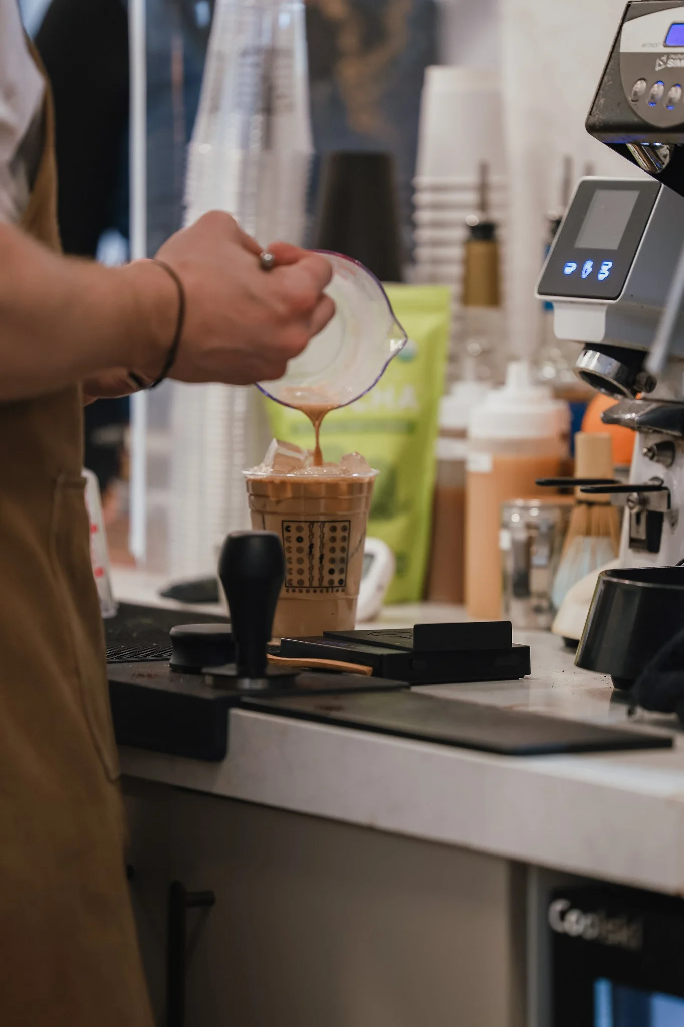 A barista making a chocolate drink at a coffee shop, pouring chocolate into a cup.