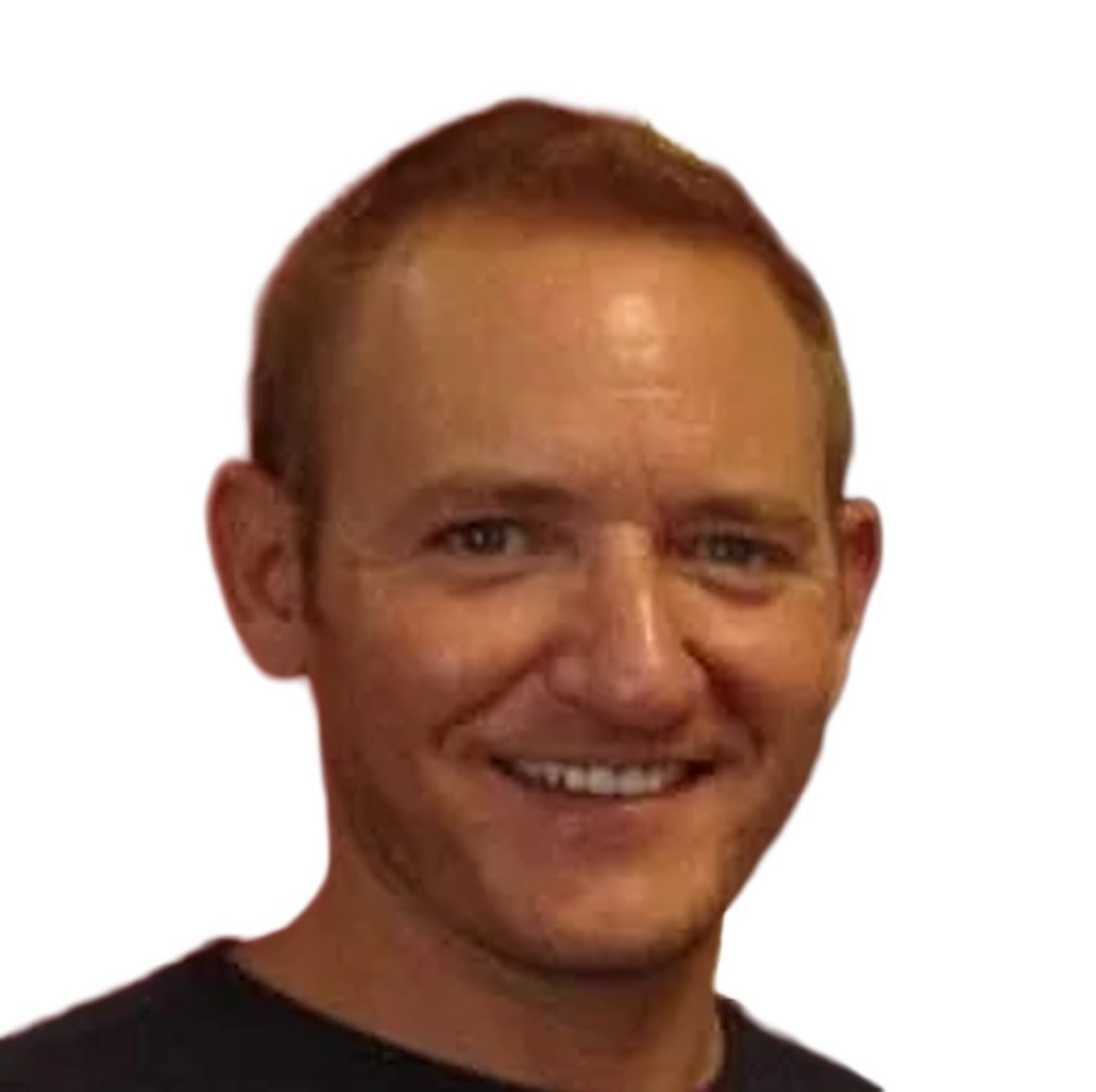 Smiling man with short red hair and light skin, wearing a black shirt, against a plain dark background.