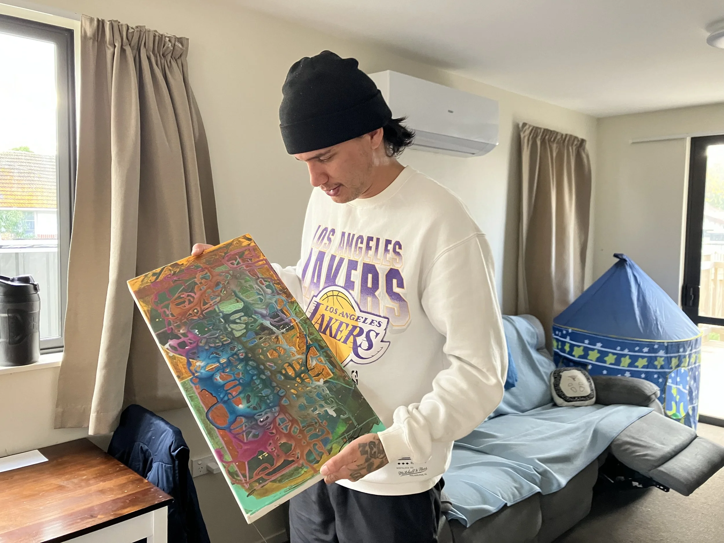 J holds his painting, an abstract piece with greens, reds, blues and oranges
