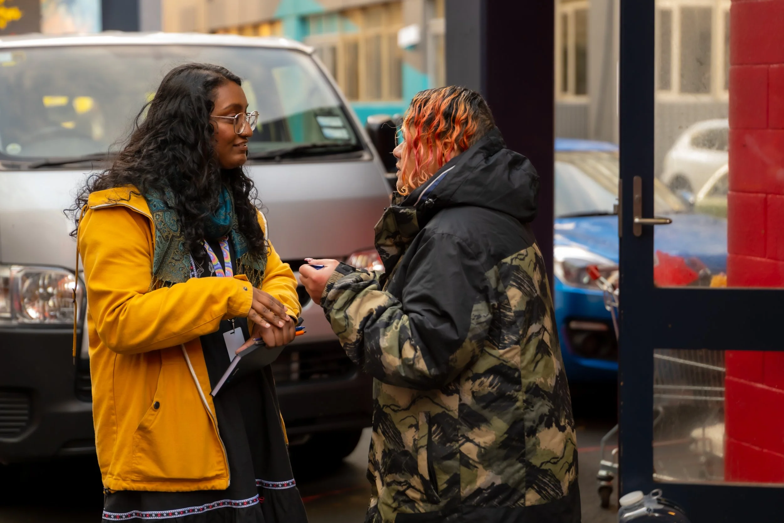 A DCM Kaimahi in a yellow jacket and whānau in a camo puffer jacket are engaged in conversation