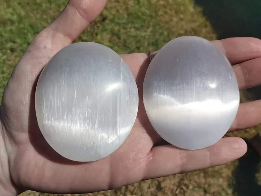 A hand holding two large Selenite soap-stones, each roughly the size of the entire palm.