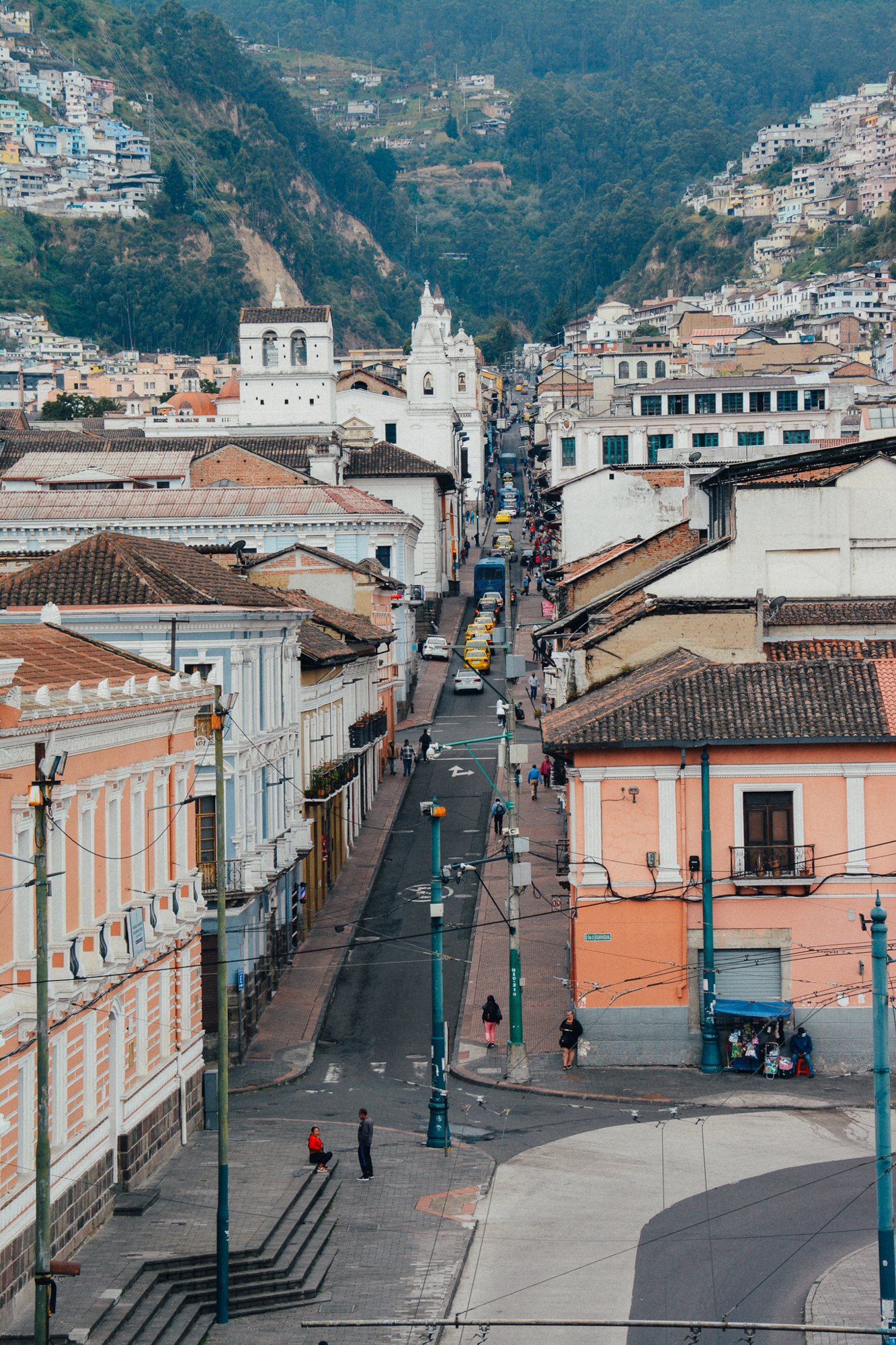 Rue en pente à Quito, bâtiments coloniaux et montagnes en arrière-plan.