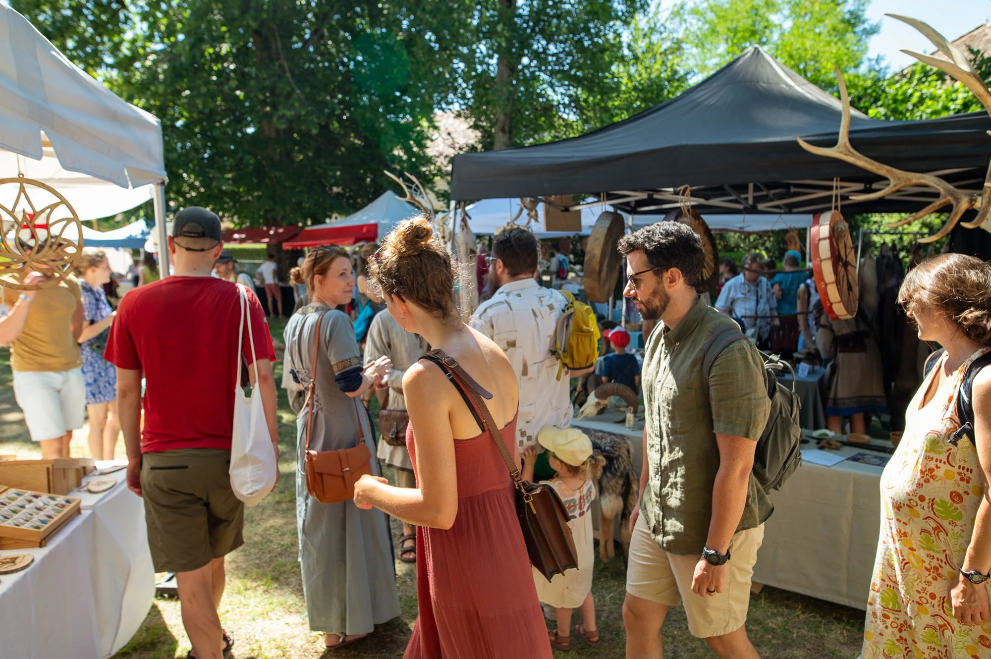 Les gens visitent un marché en plein air lors de la fête médiévale de La Sarraz, avec des stands d’objets artisanaux installés sous des tentes, lors d’une journée ensoleillée.