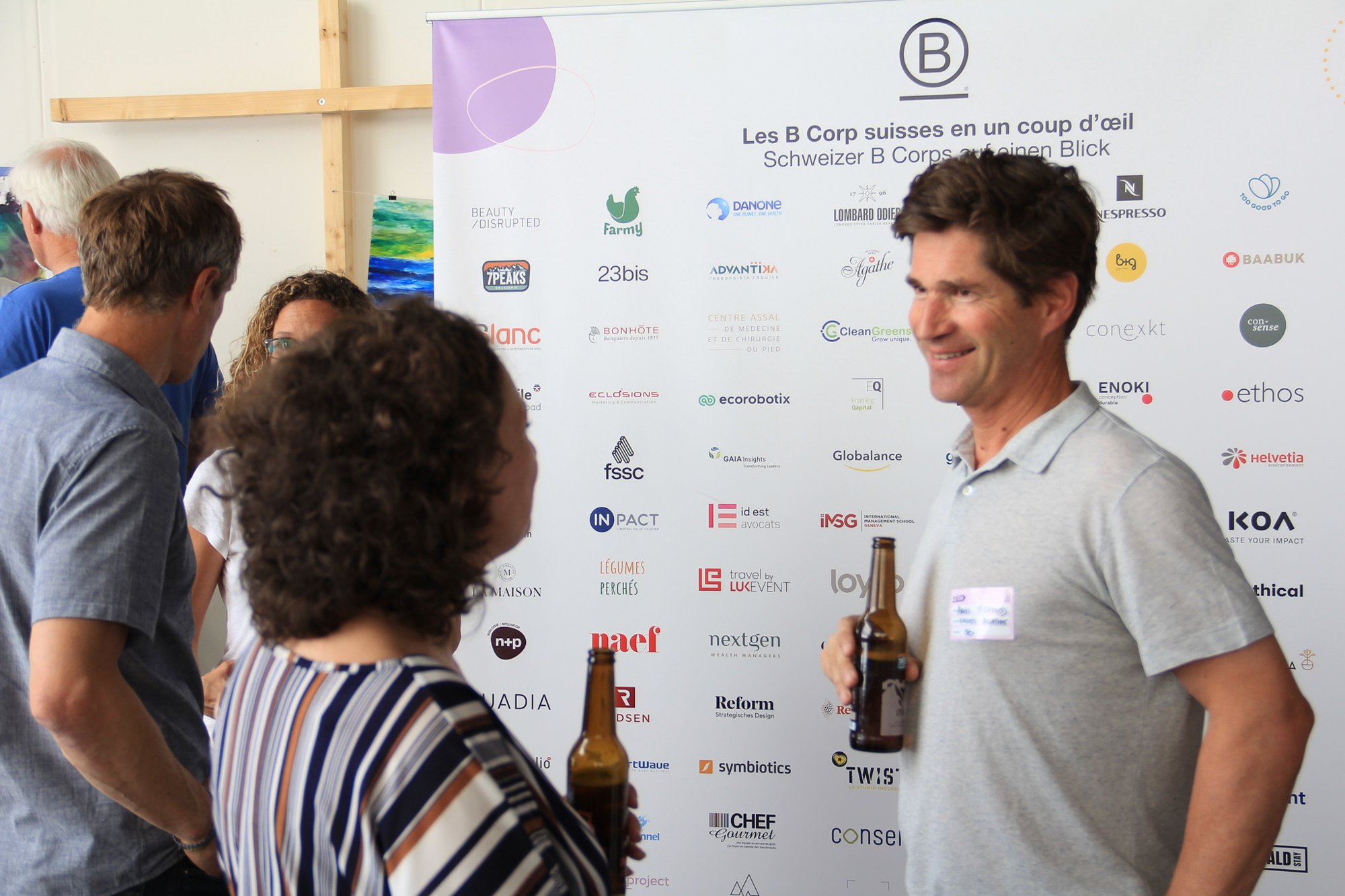 Groupe de personnes discutant lors d'un événement professionnel devant un panneau avec de nombreux logos d'entreprises.