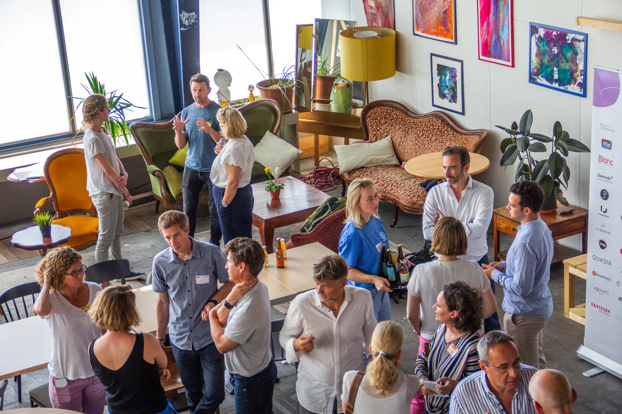 Une réunion ou un événement social dans un espace intérieur où plusieurs personnes discutent, avec des œuvres d'art modernes sur le mur et un mobilier vintage.