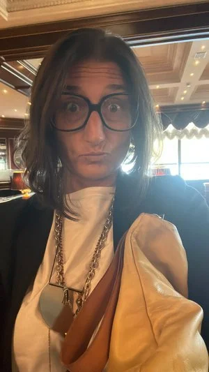 Persona con occhiali grandi in un ambiente interno elegante.