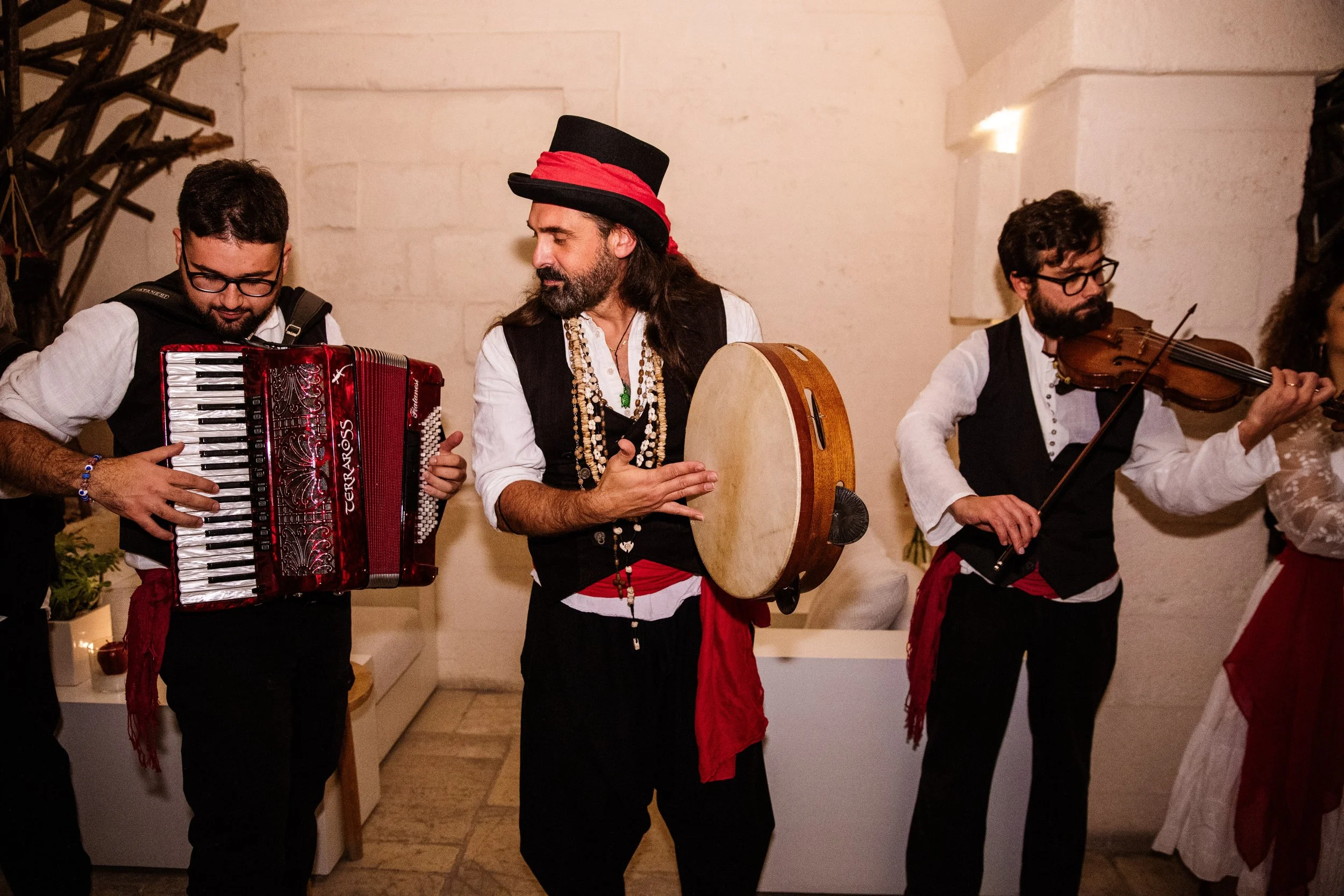 Gruppo musicale tradizionale composto da tre uomini che suonano rispettivamente una fisarmonica, un tamburello e un violino, vestiti in abiti folk.
