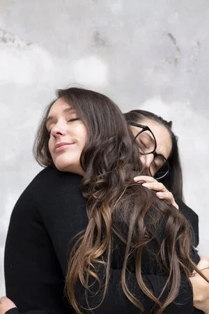 Due persone che si abbracciano con affetto, vestite di nero.