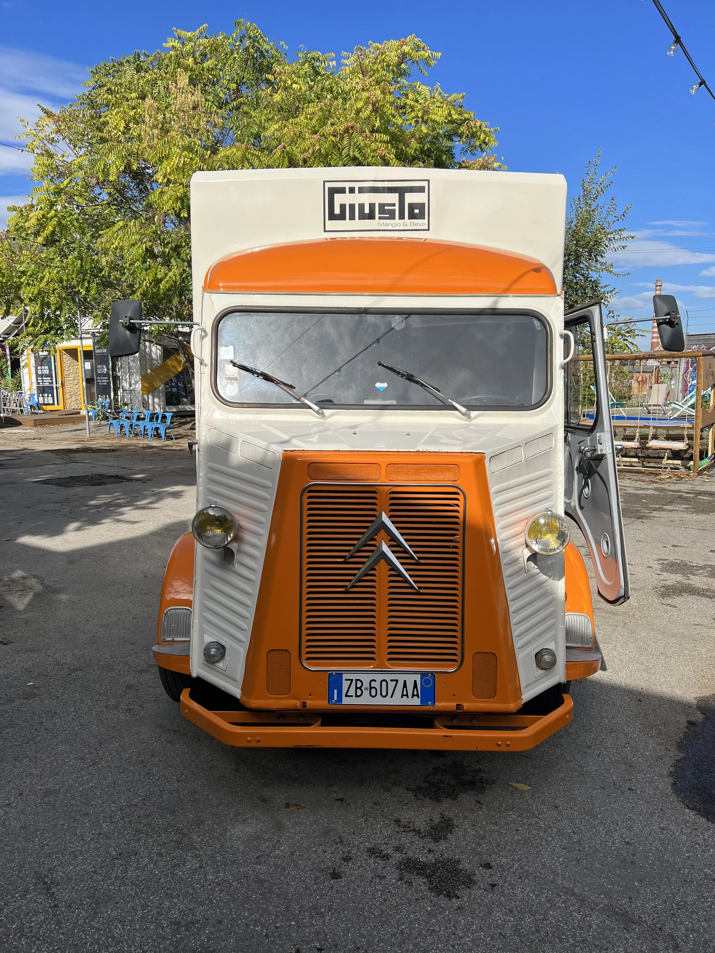 Furgone Citroën H arancione e bianco parcheggiato su strada, con alberi sullo sfondo.