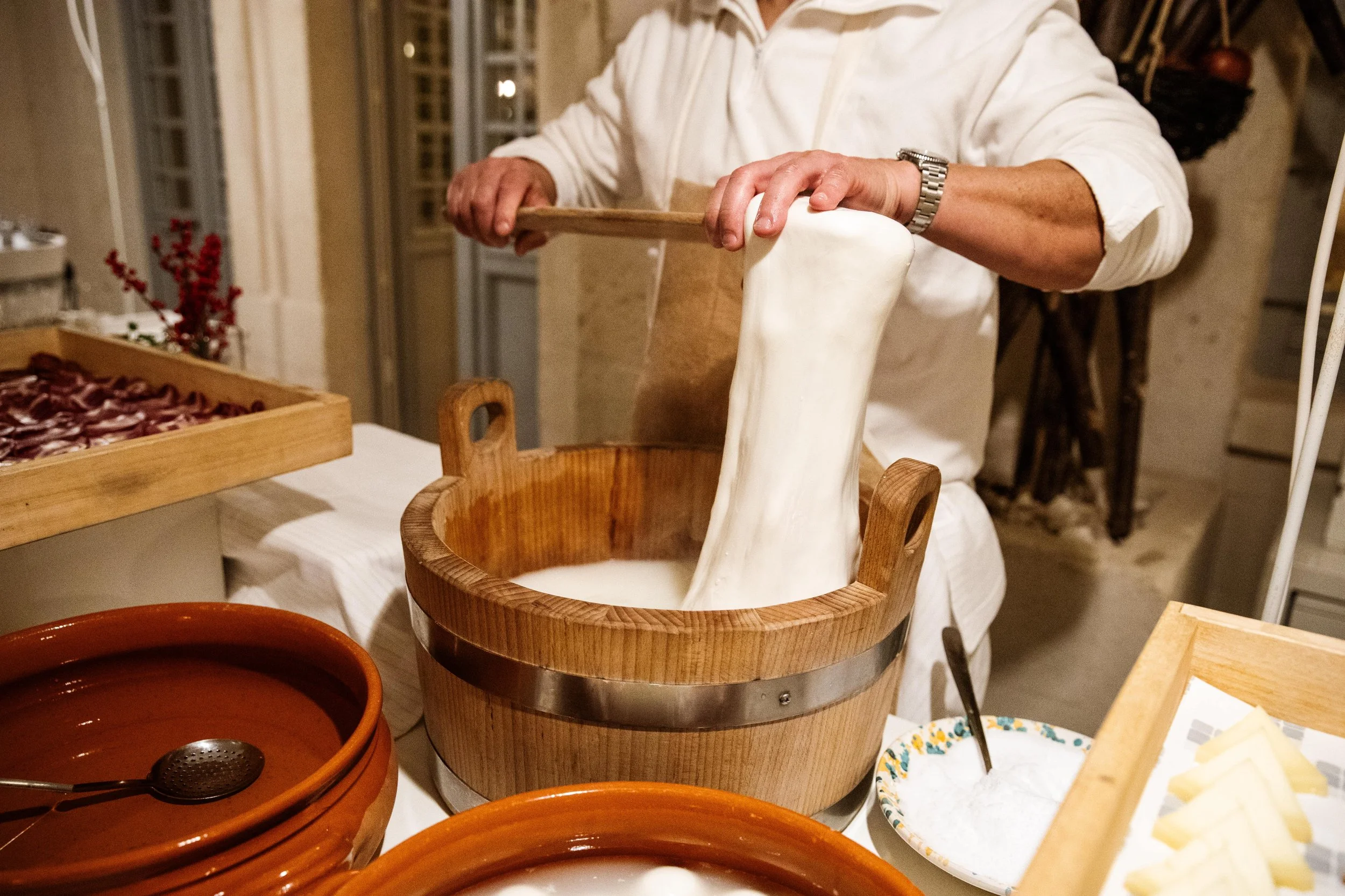 Preparazione artigianale della mozzarella in un ambiente tradizionale, con una persona che lavora il formaggio in una ciotola di legno.