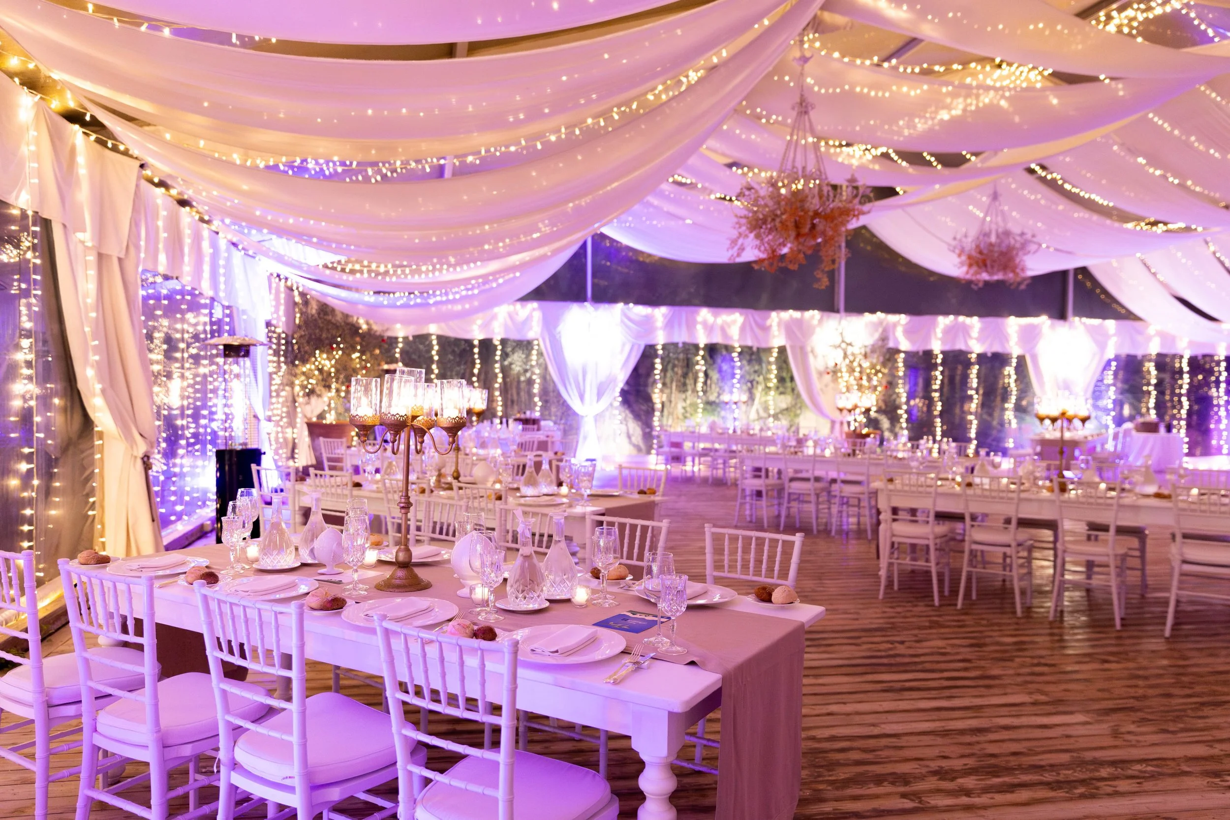 Interno di una serra allestita per un evento con tavoli apparecchiati e luci soffuse.